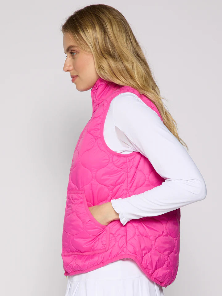 Woman wearing a pink quilted vest over a white long-sleeve shirt on a light gray background