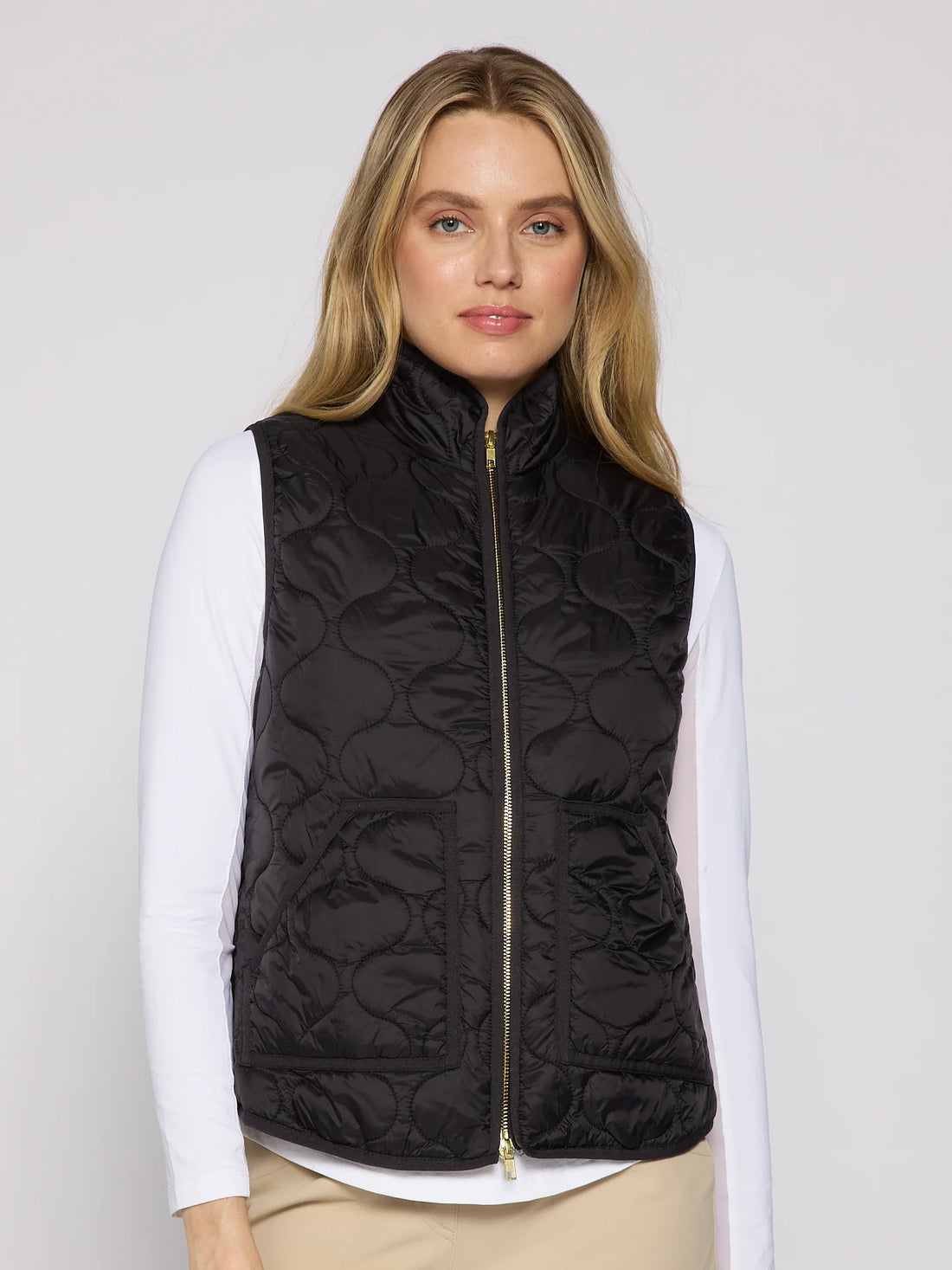 Woman wearing a black quilted vest over a white shirt on a plain background